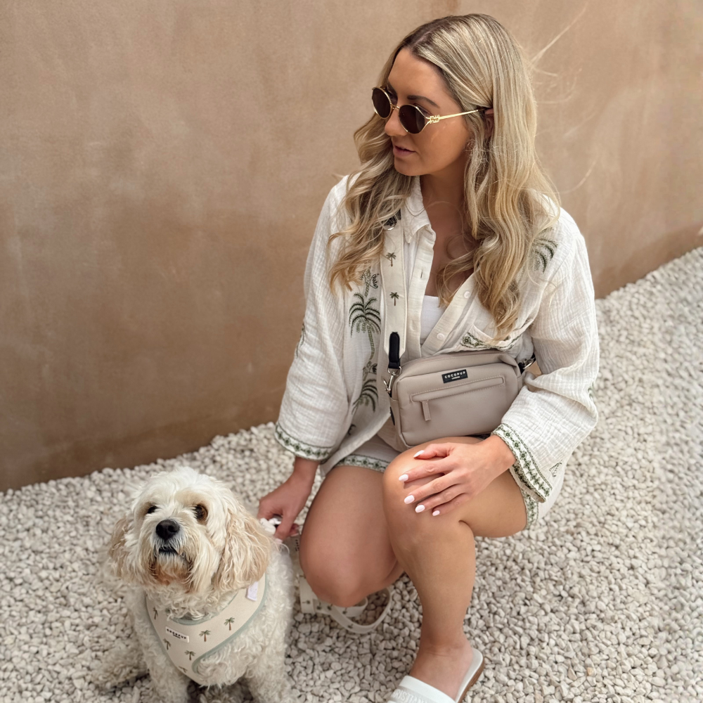A woman crouches next to her small white dog, both wearing items with a palm tree print.