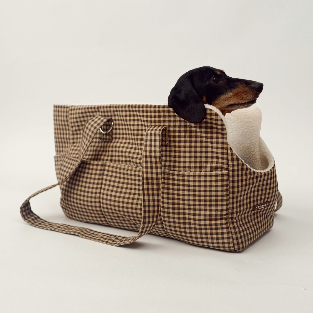 A black and tan dachshund sits inside a brown and beige gingham tote bag on a white background.