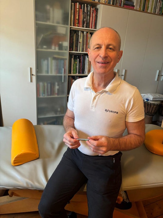 A person in a white shirt holding an item, near a massage table in a room.