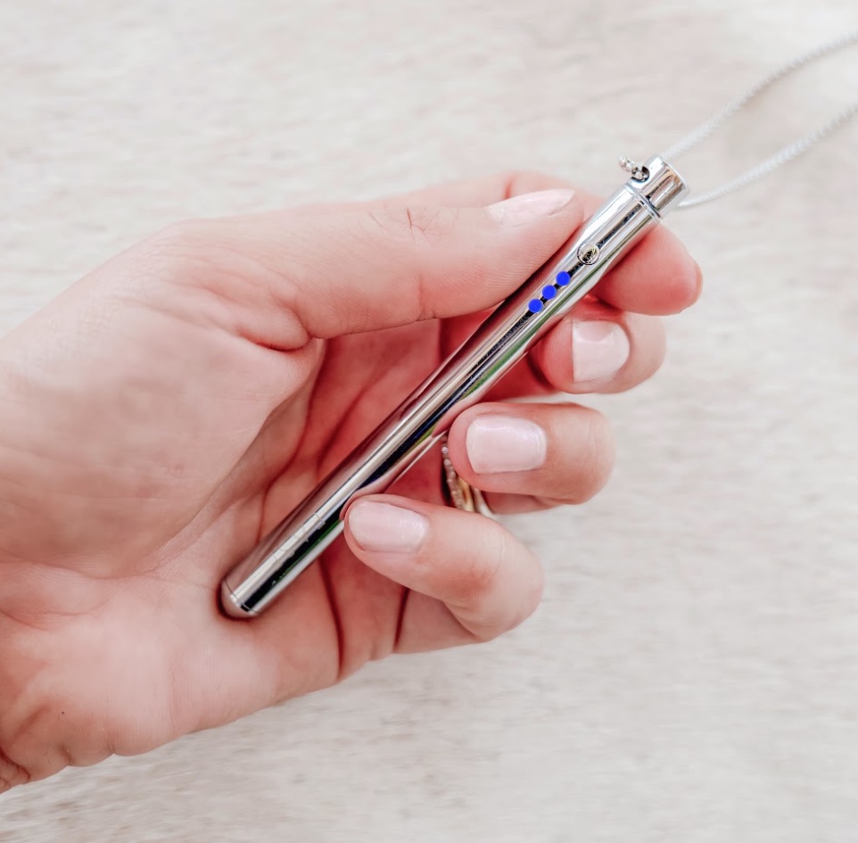 Hand holding a silver pen with blue dots and a chain.