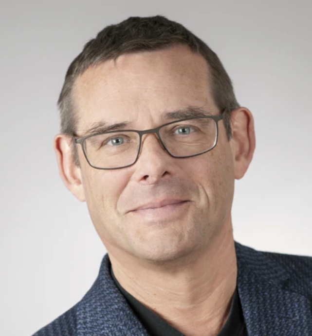 A person wearing glasses and a blue jacket, smiling slightly.