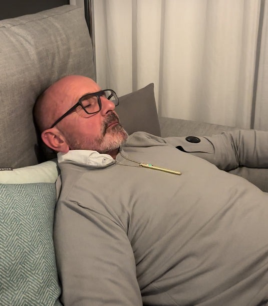 A person in glasses is sleeping on a gray sofa.
