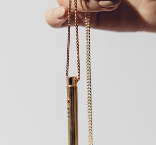 Hand holding a gold cylindrical pendant on a chain.