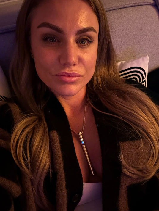 A person with long hair and a pendant is sitting on a couch.
