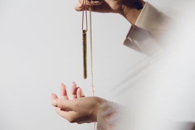 Hands holding a gold pendulum against a light background.