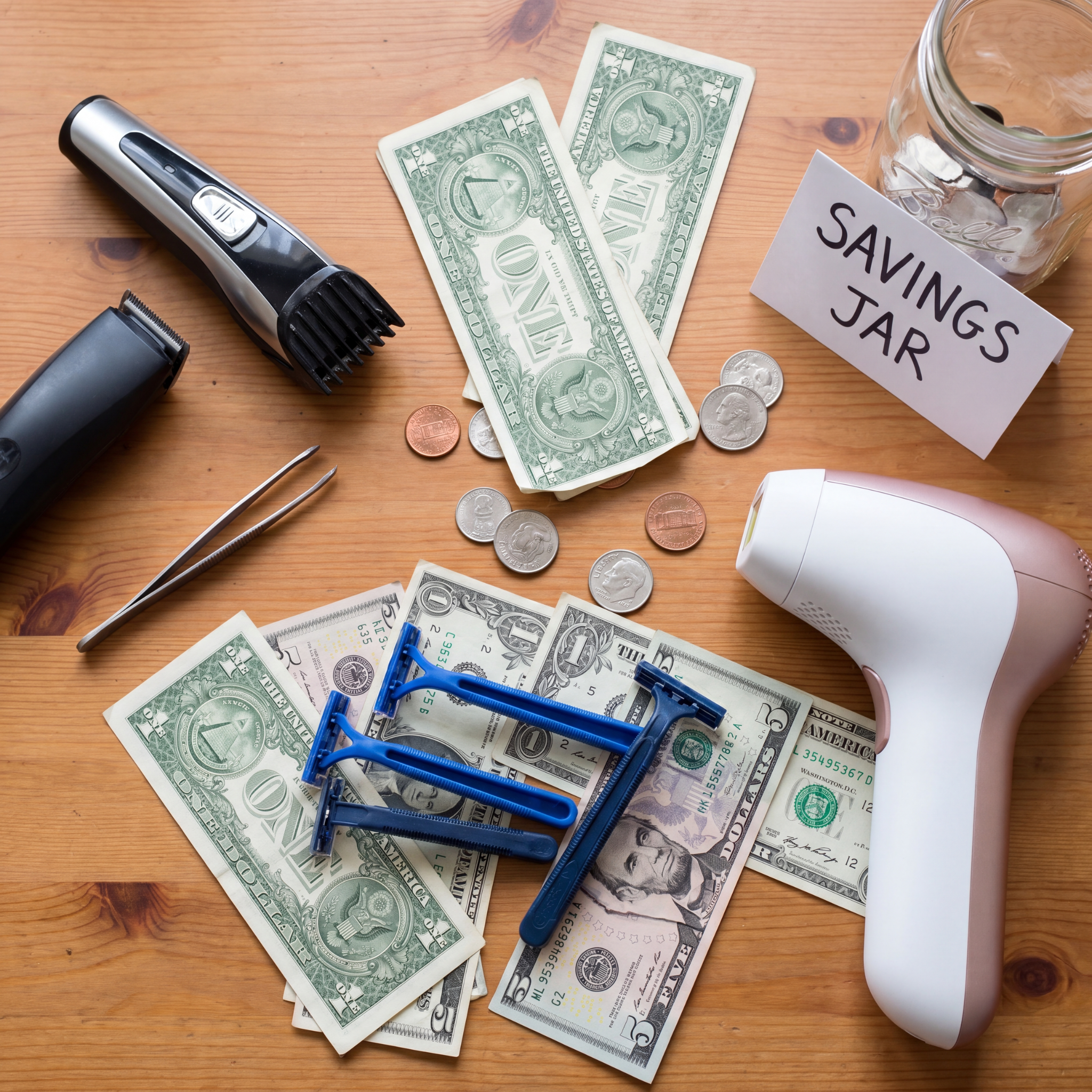 Hair removal tools like razors and clippers scattered on a wooden table with US currency and a savings jar.