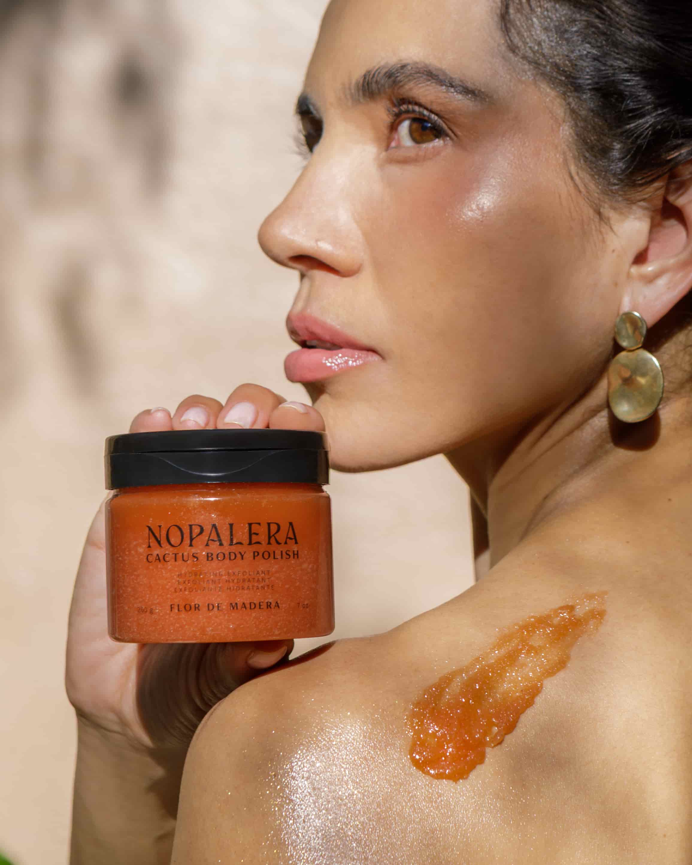 Mujer sosteniendo el Exfoliante Corporal de Cactus Flor de Madera de Nopalera junto a su piel exfoliada.