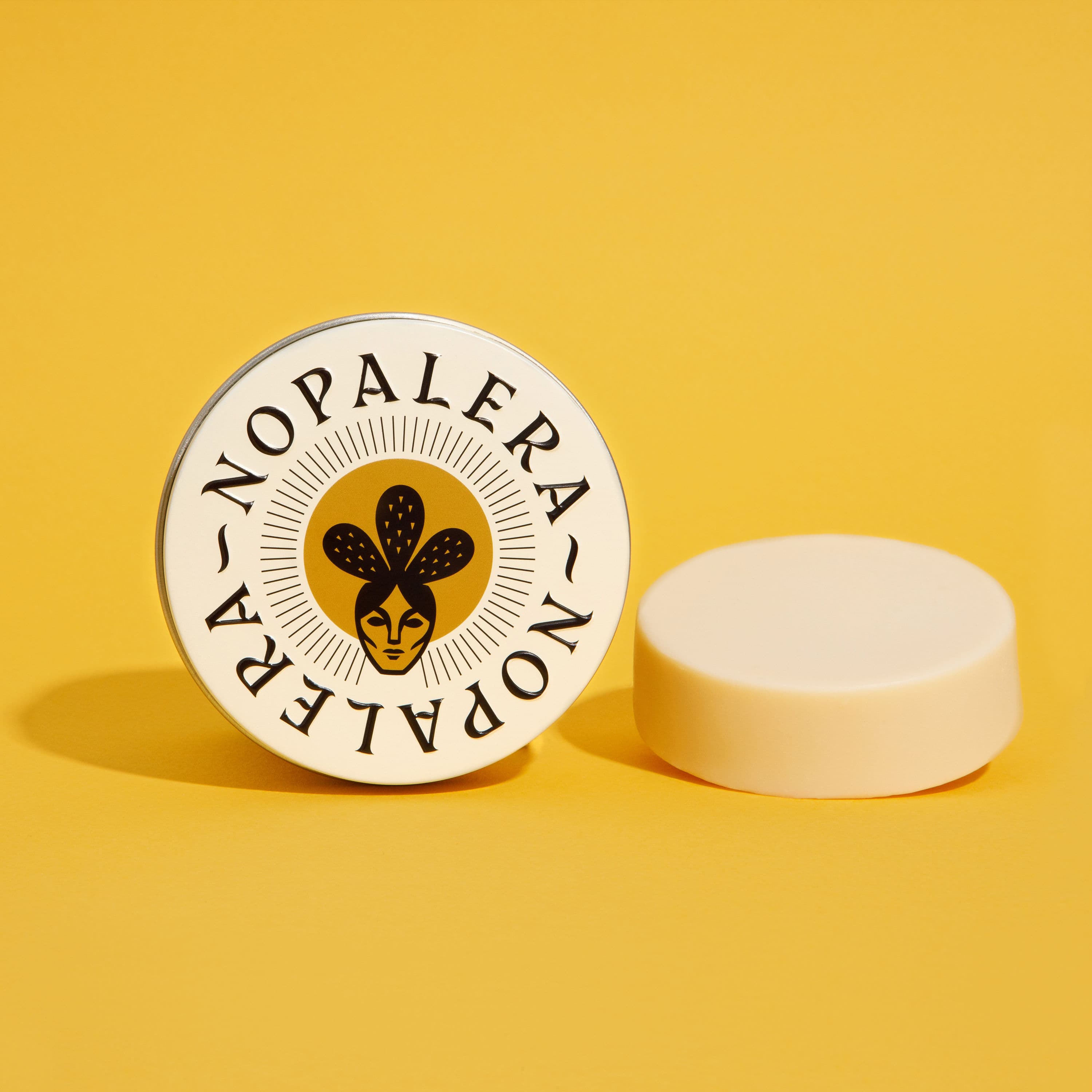 A round Nopalera brand tin and a solid lotion bar on a yellow background.