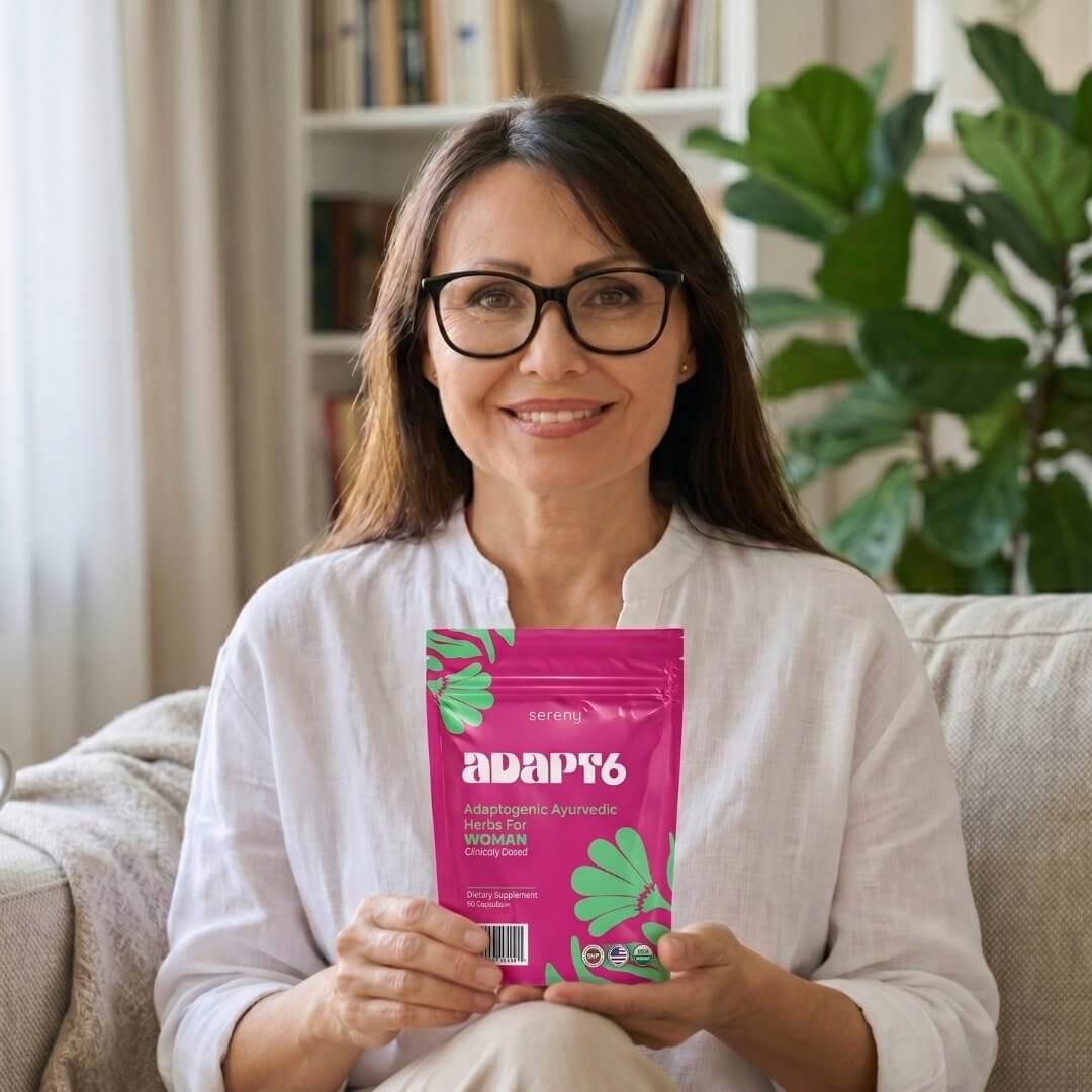 A smiling woman with glasses sits on a couch holding a pink pouch of Sereny Adapt6.