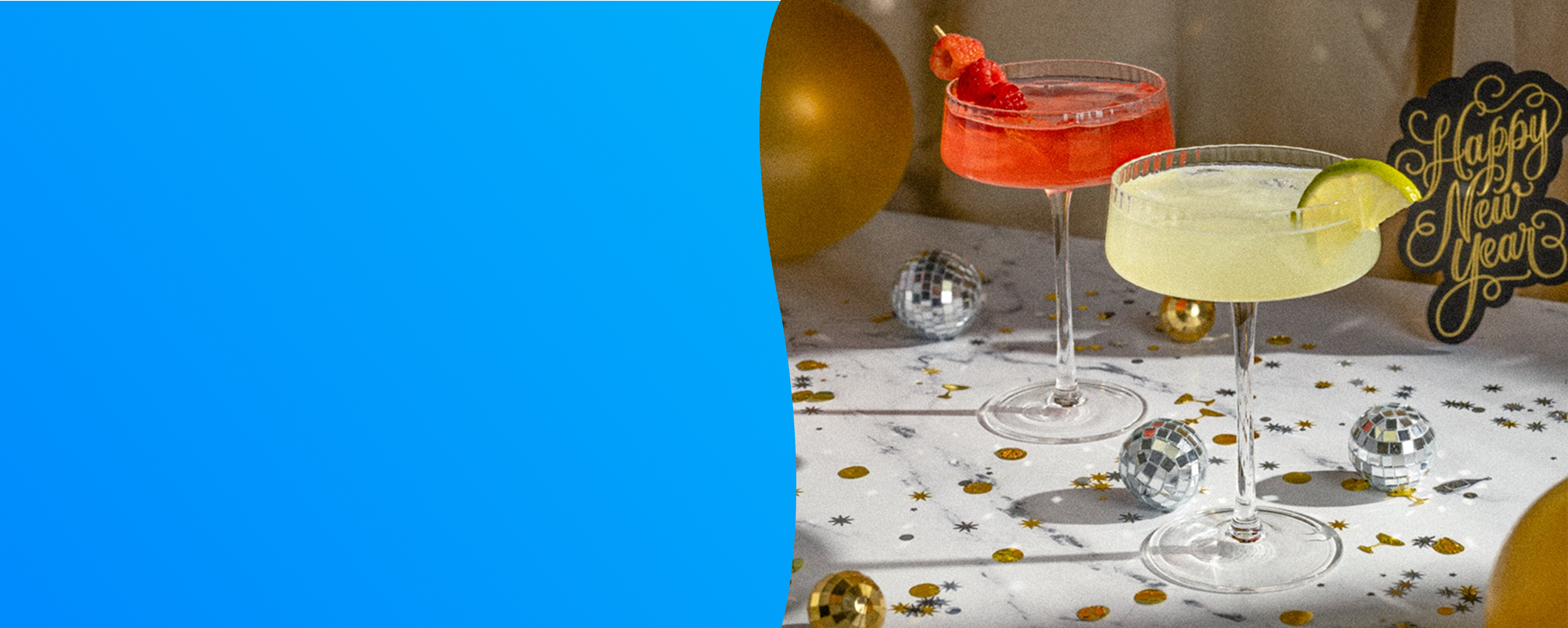 Two cocktails and decorations with a 'Happy New Year' sign on a festive table.