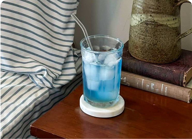 A glass of blue drink with ice and a straw on a table beside books.