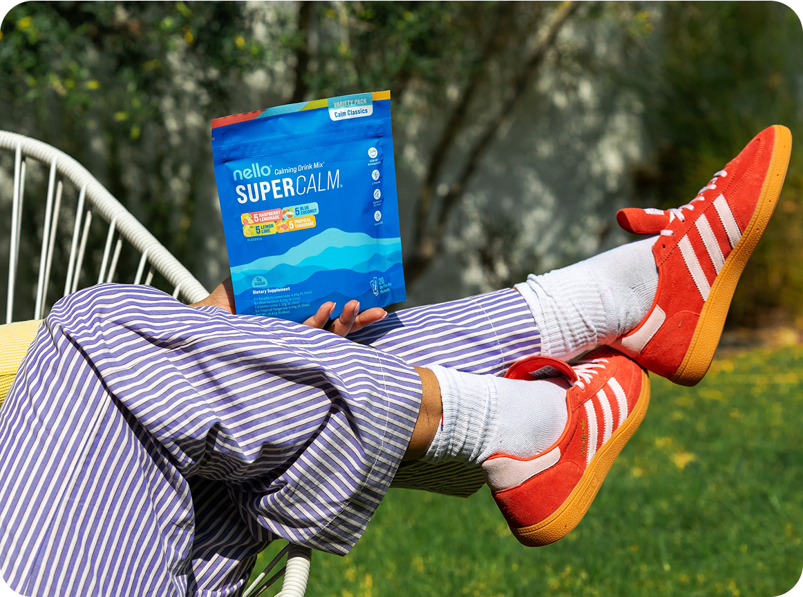 Person wearing red shoes, striped pants holding a SuperCalm drink mix packet.