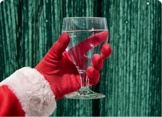 Santa-like gloved hand holding a glass of water against a green background.