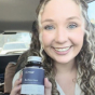 Person in a car holding a bottle, smiling at the camera.