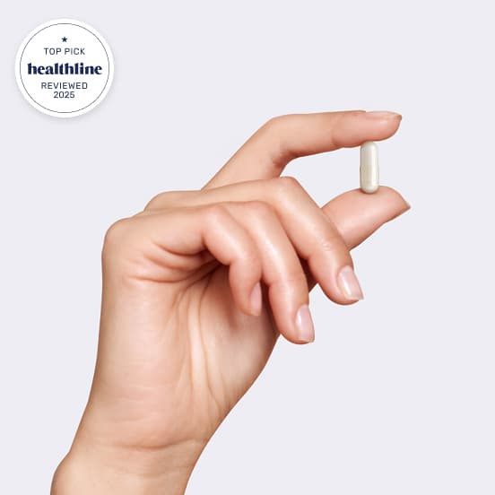 Hand holding a small white capsule against a plain background.