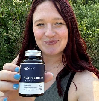 Person holding a bottle of Ashwagandha supplement outdoors.