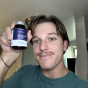 Person holding a small bottle with a blue label, smiling at the camera.