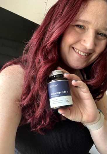 Person with red hair holding a bottle labeled Ashwagandha, smiling.