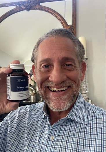 Smiling man holding a bottle labeled 'Ashwagandha' in front of a mirror.