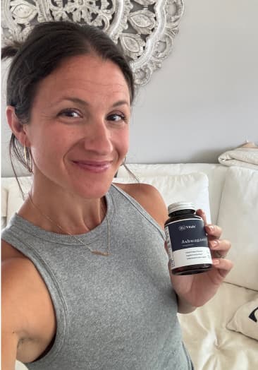 Person holding a bottle labeled 'Ashwagandha' in a living room.
