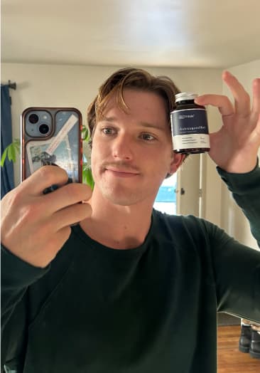 Person taking a selfie holding a small bottle in a room.