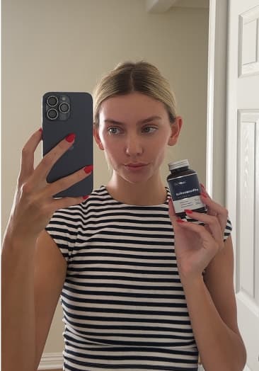 Person taking a mirror selfie holding a bottle, wearing a striped shirt.