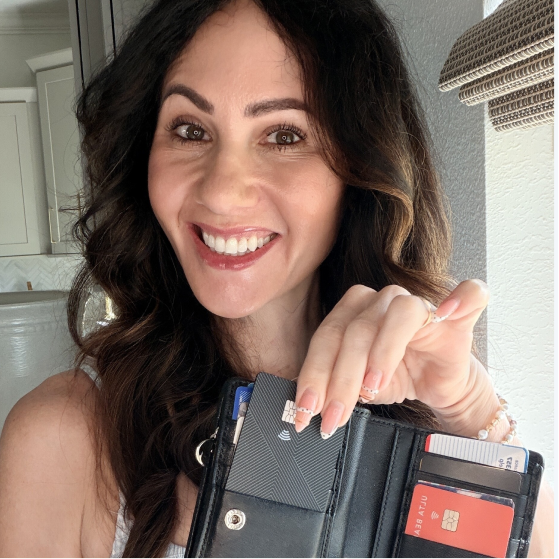 A smiling woman with long brown hair holds open a black wallet, pulling out a credit card.
