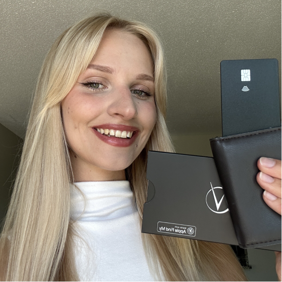 A smiling blonde woman holds a dark brown wallet with a black card and packaging.