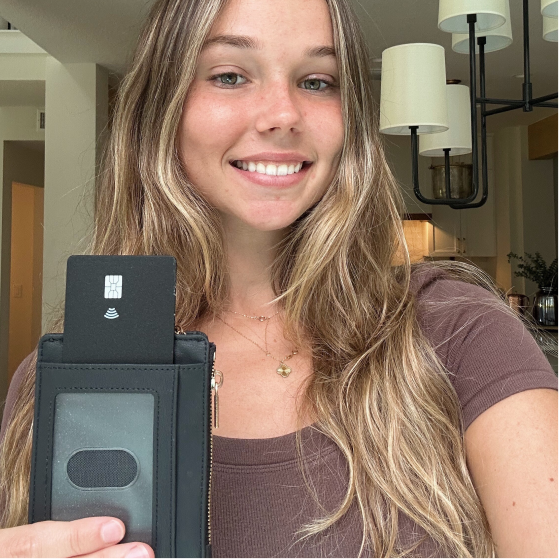 A smiling woman holds up a black wallet with a credit card sticking out of the top.
