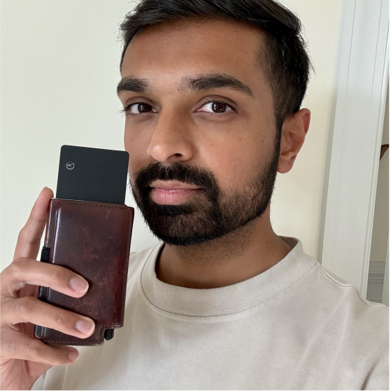 A man with a beard holds a brown leather wallet with a black card partially ejected from it.