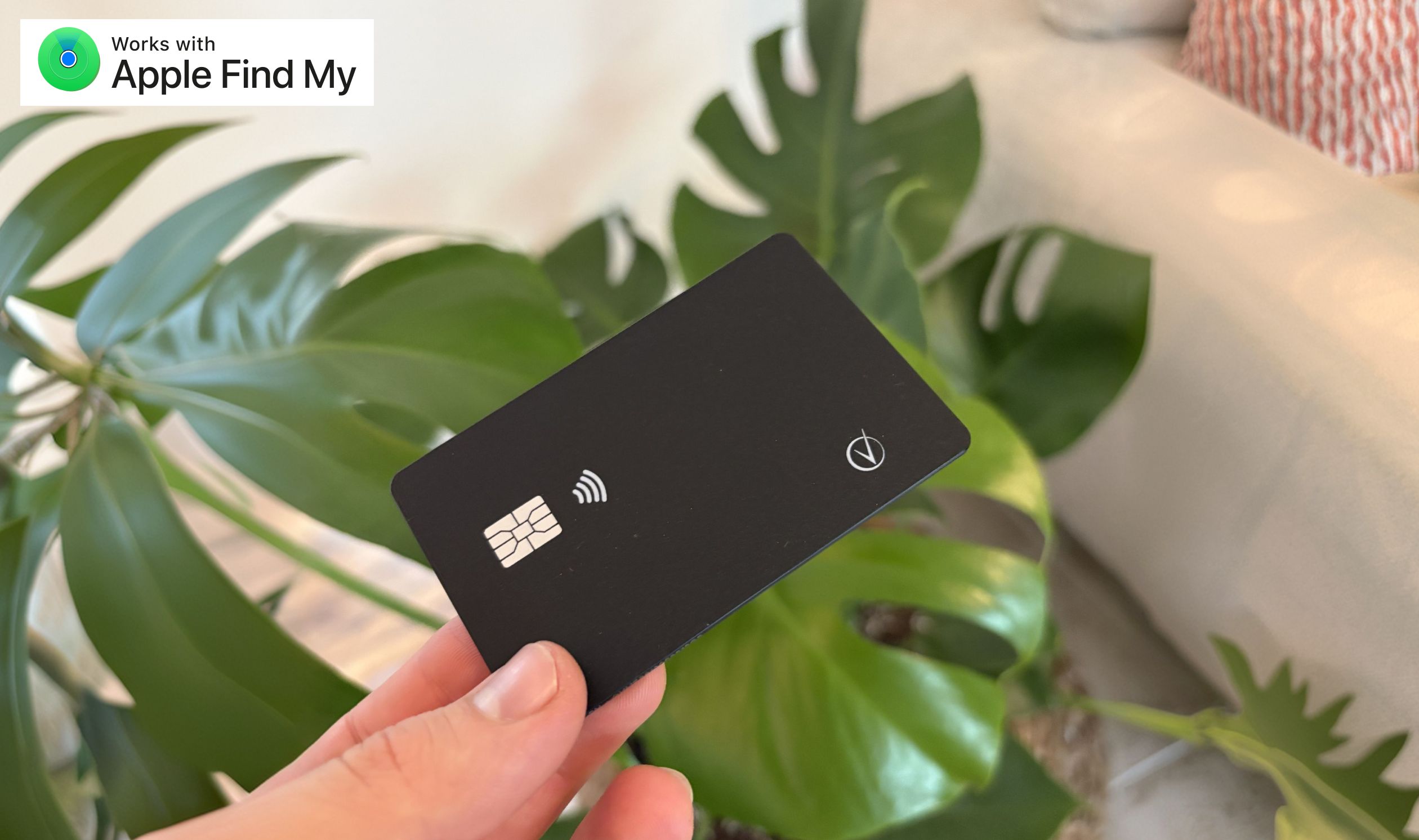 A hand holds a black smart card in front of a leafy green plant.