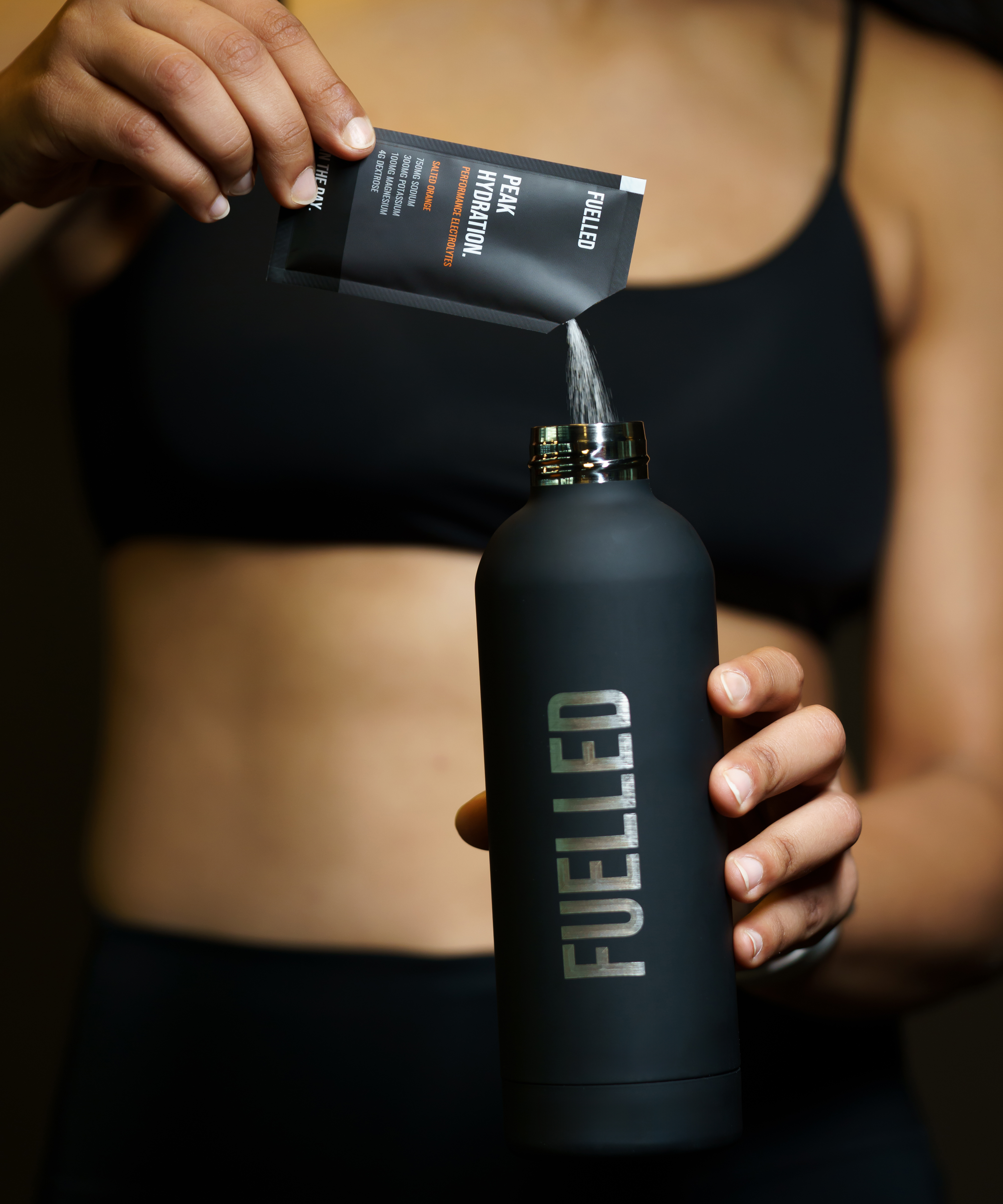 Person pouring powder from packet into a black bottle labeled 'FUELLED.'