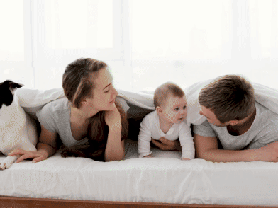 Family with baby and dog lying on bed together.