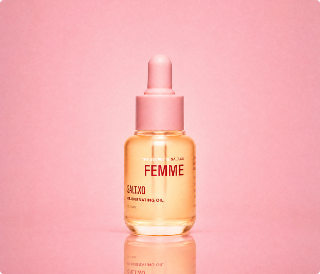 A glass bottle of Salt.XO Femme Rejuvenating Oil with a pink dropper cap against a pink background.