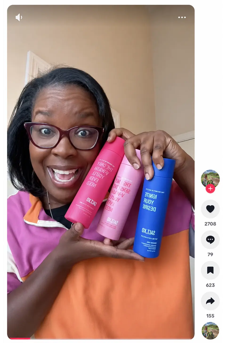 A woman with glasses smiles while holding three colorful bottles of Salt XO products.