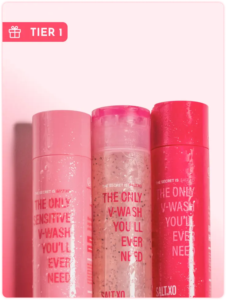 Three different pink bottles of V-Wash by Salt.xo stand side-by-side against a pink background.