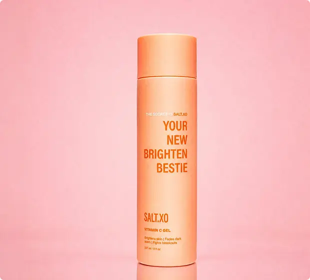 A peach-colored bottle of Salt.XO Vitamin C Gel labeled 'Your New Brighten Bestie' against a pink background.