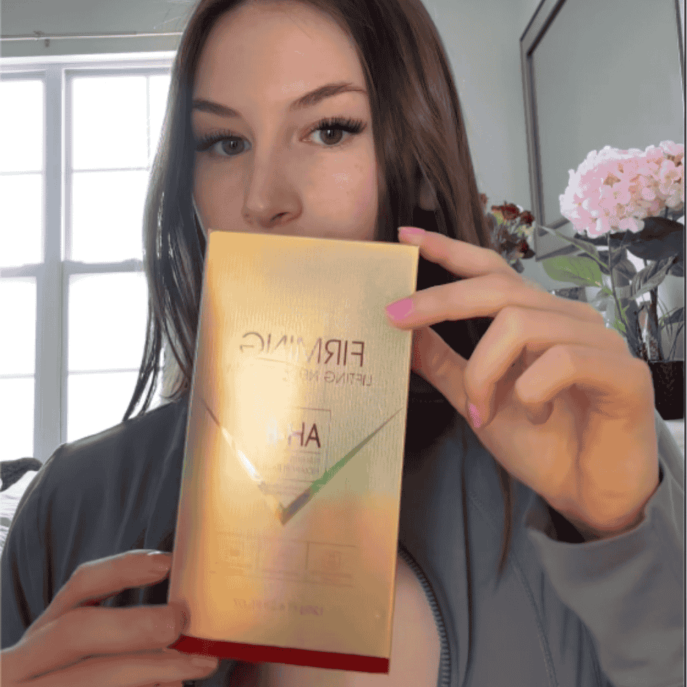 Person holding a gold skincare product box in front of their face.