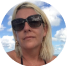 A close-up, circular photo of a blonde woman in sunglasses, with a cloudy sky behind her.