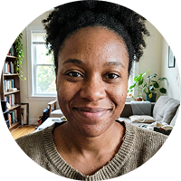 A close-up, circular photo of a smiling Black woman with natural hair, indoors.