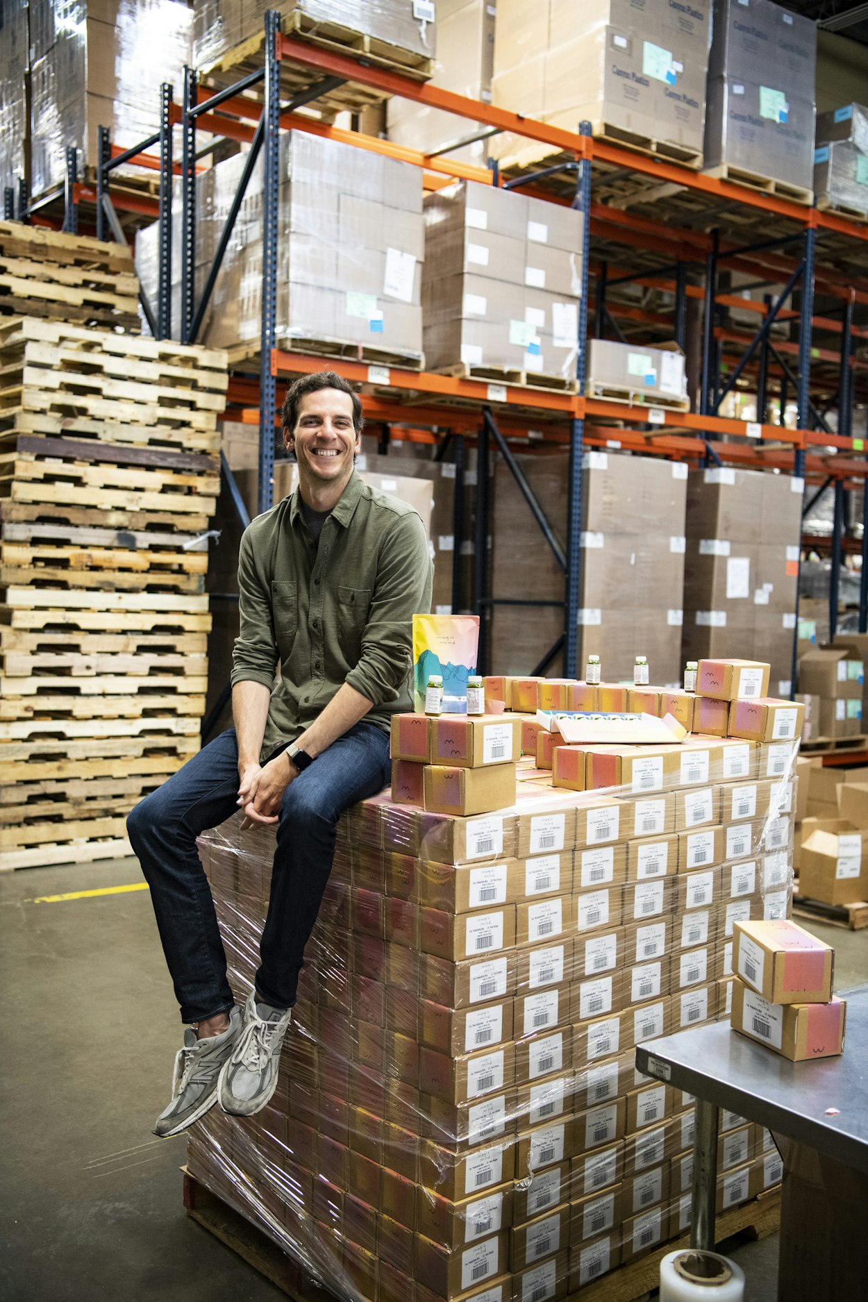 Man sitting on stacked boxes in a warehouse, smiling.