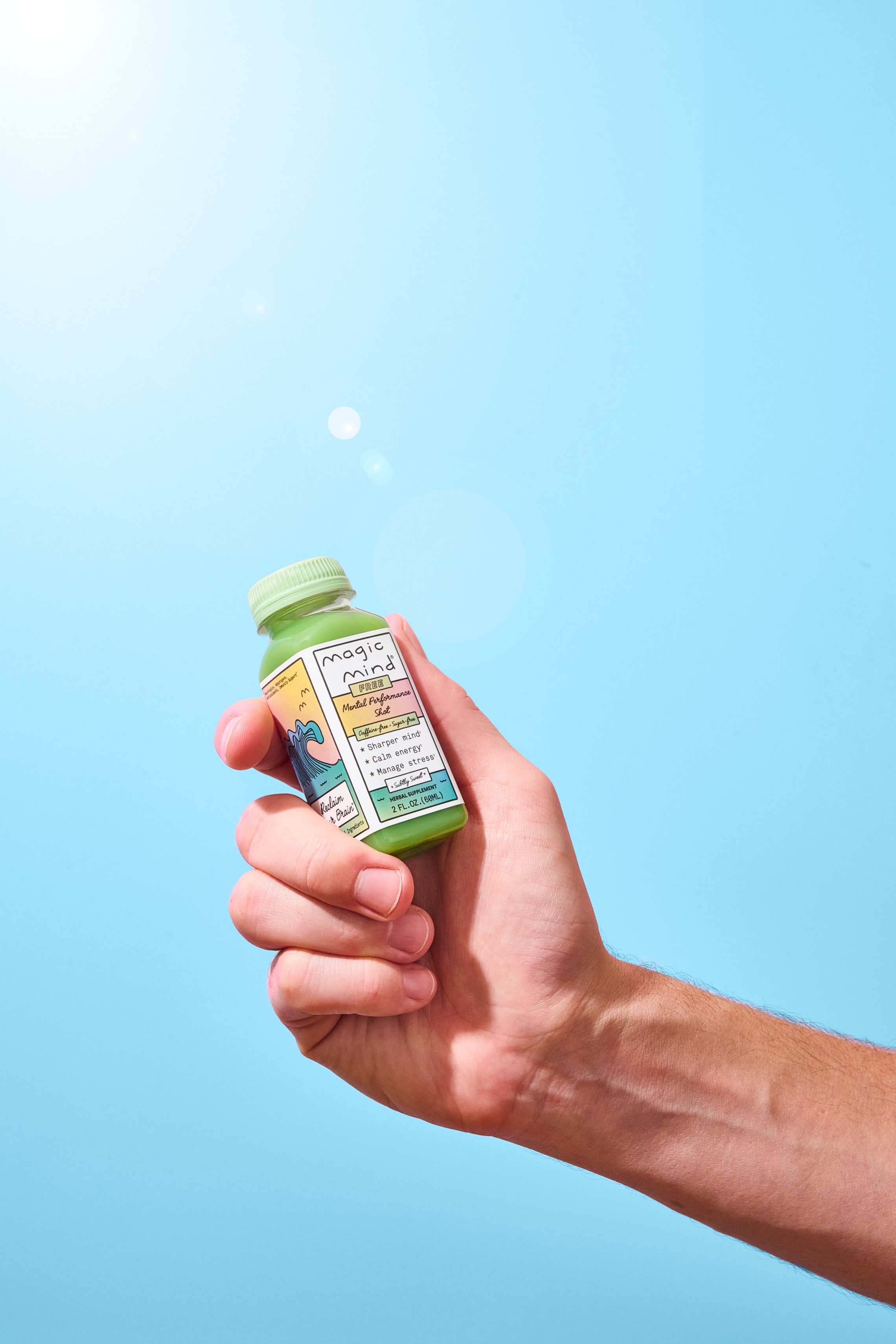 Hand holding a small green bottle labeled 'Magic Mind' against a blue background.