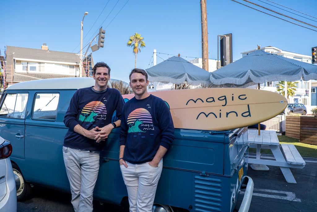 Two people standing beside a vintage van with surfboards.