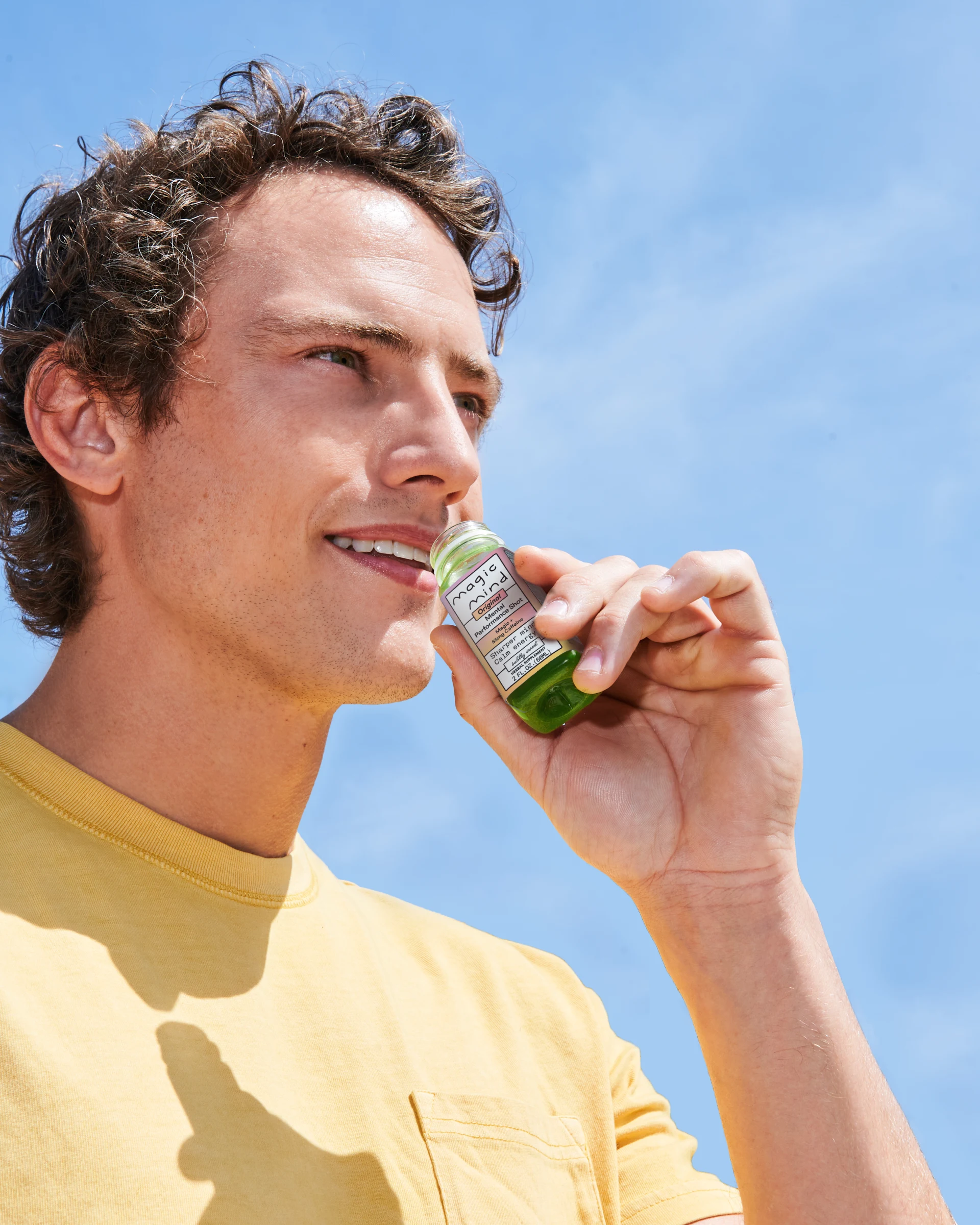 Man holding a small green bottle under blue sky.