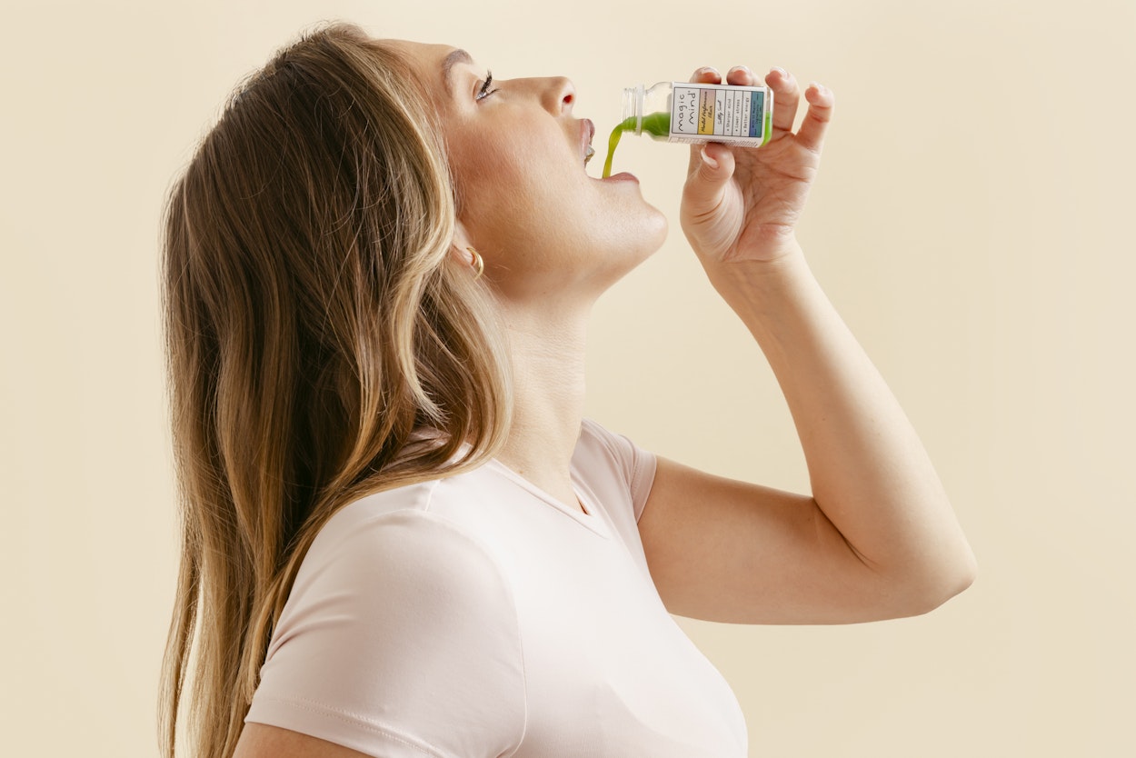 A person drinks from a small bottle filled with green liquid.