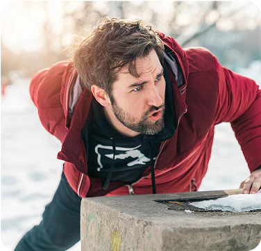 Man in red jacket leaning over a stone surface in snowy outdoors.