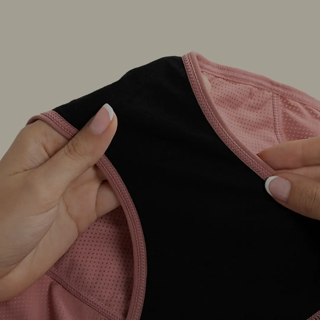 A person's hands hold open a pair of pink mesh underwear, showing the black gusset.