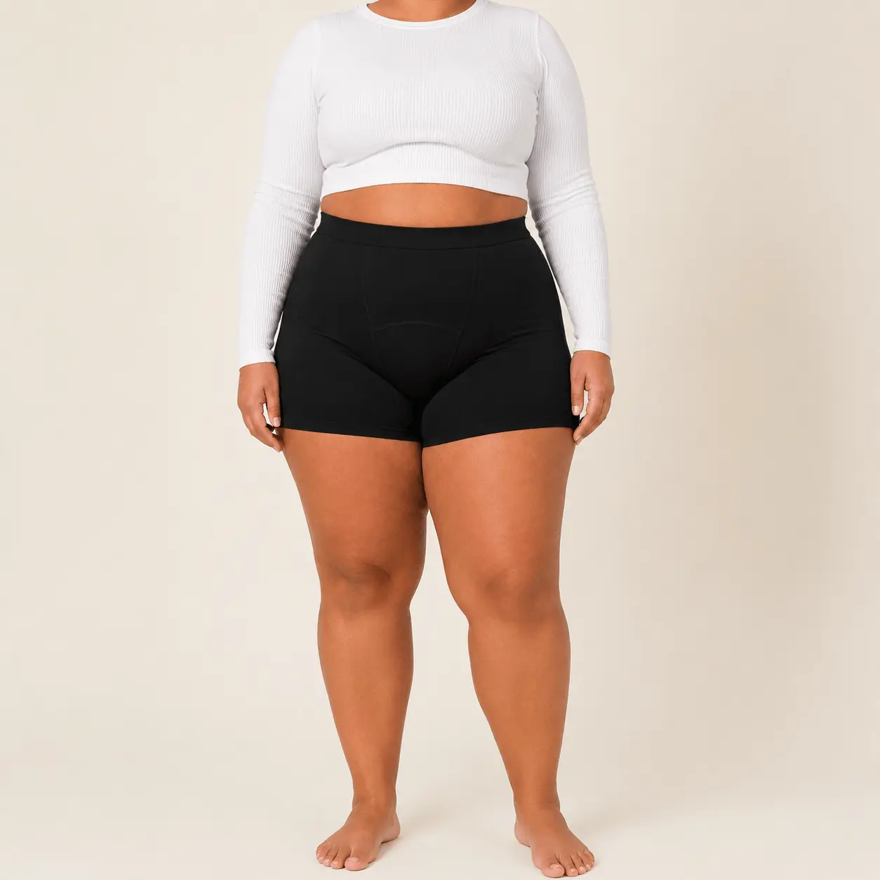 A person stands wearing a white long-sleeved crop top and black boy shorts.