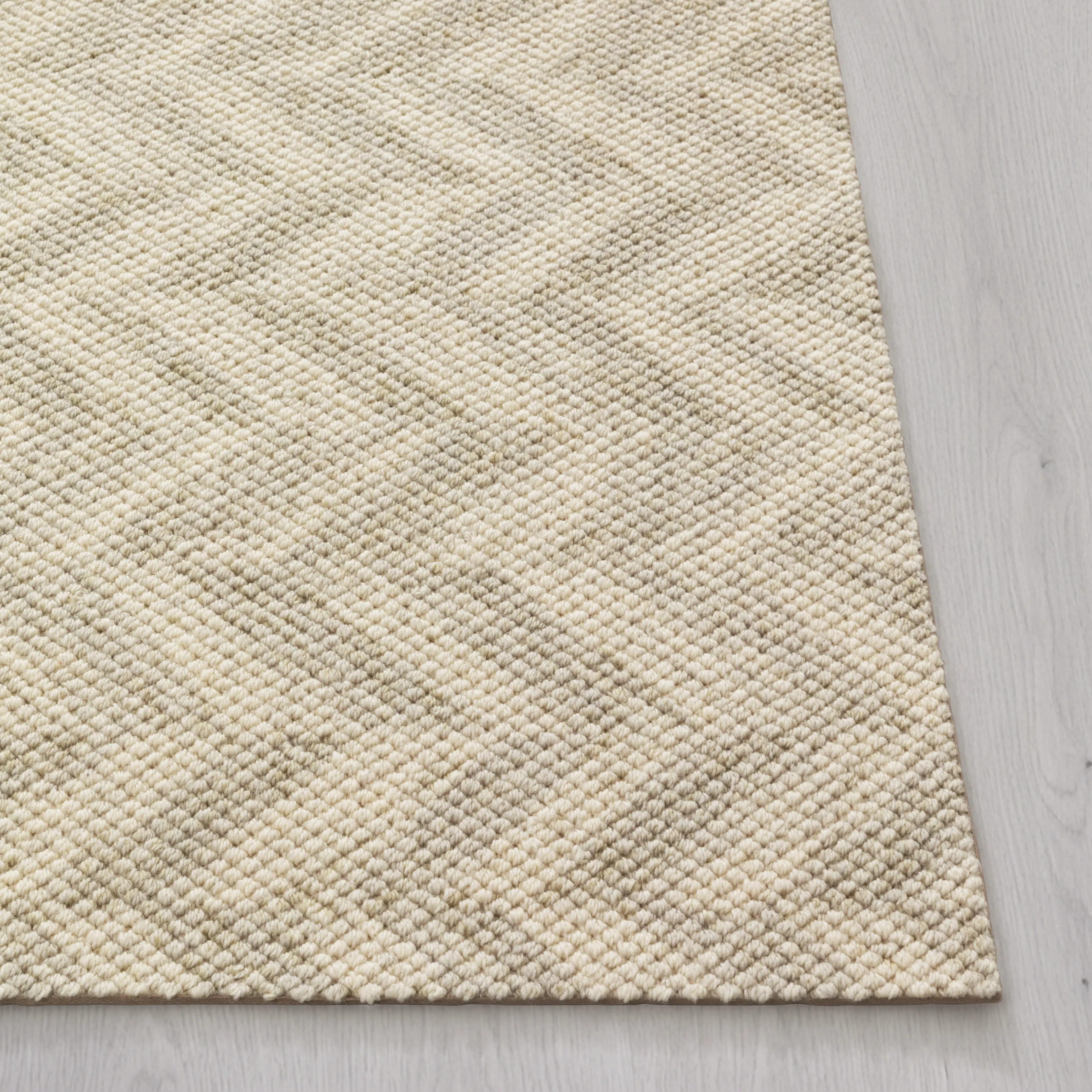 A close-up, angled view of a textured, off-white woven rug on a light gray wood floor.