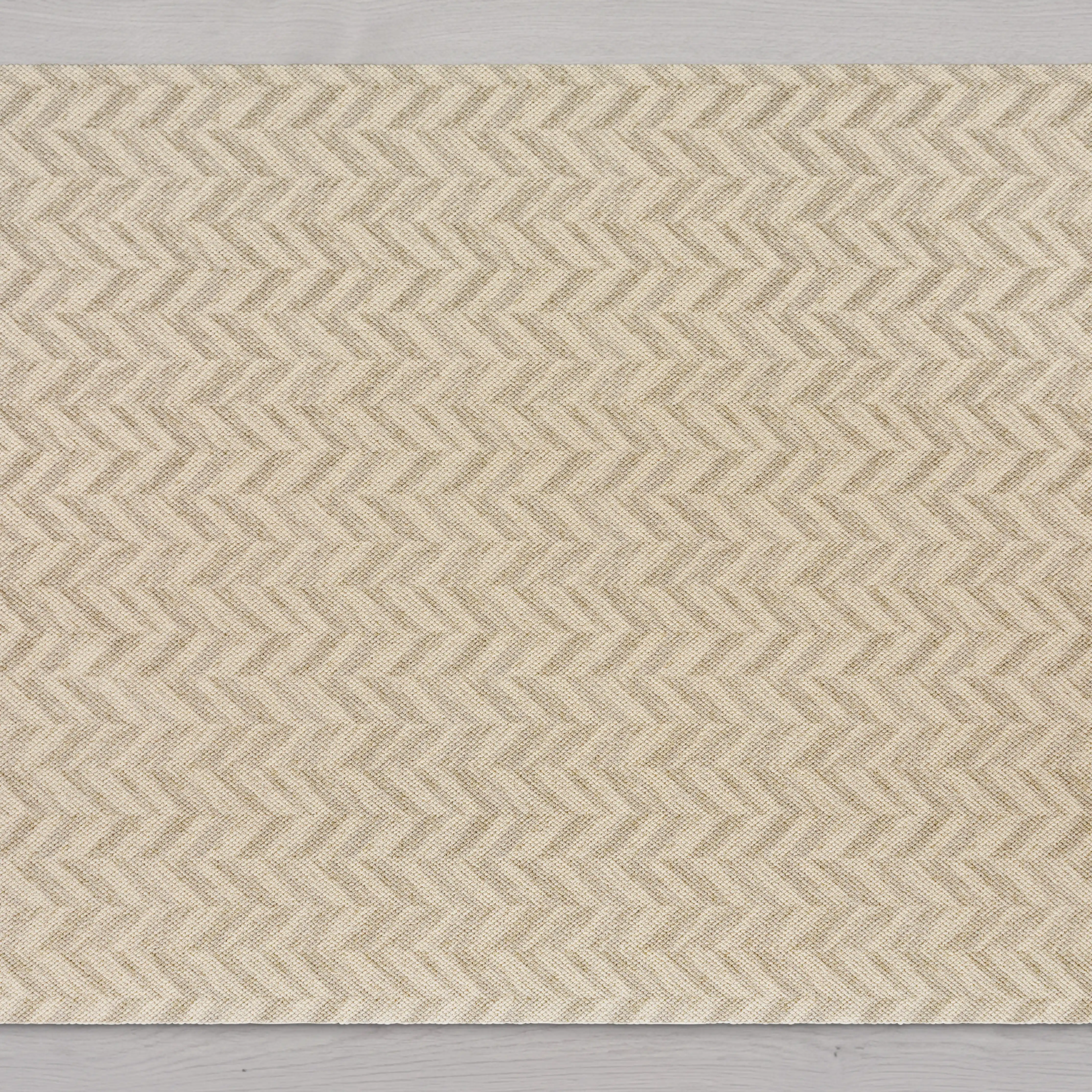 A top-down view of a beige woven rug with a chevron pattern on a light gray floor.